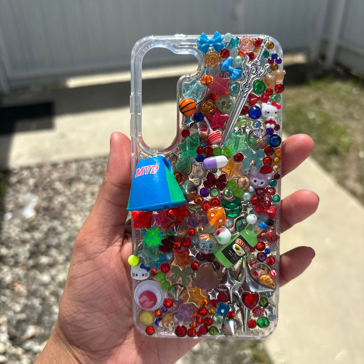 Hand holding a clear phone case with colorful beads and stickers outdoors.